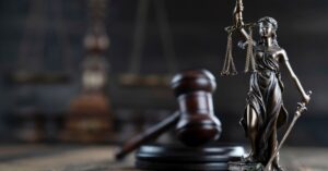 A bronze statue of Lady Justice holding scales and a sword stands in front of a gavel and block, symbolizing the importance of justice in every personal injury case, with blurred scales of justice in the background.